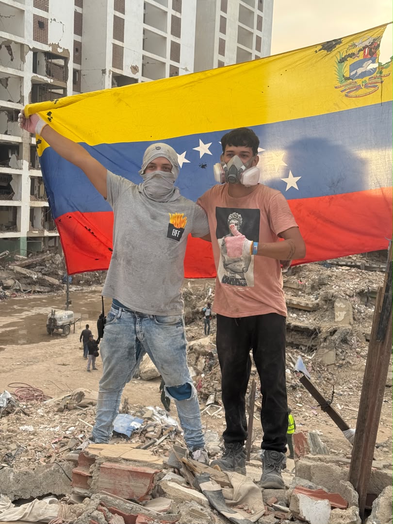 Luisito y un voluntario sosteniendo la bandera de Venezuela entre los escombros